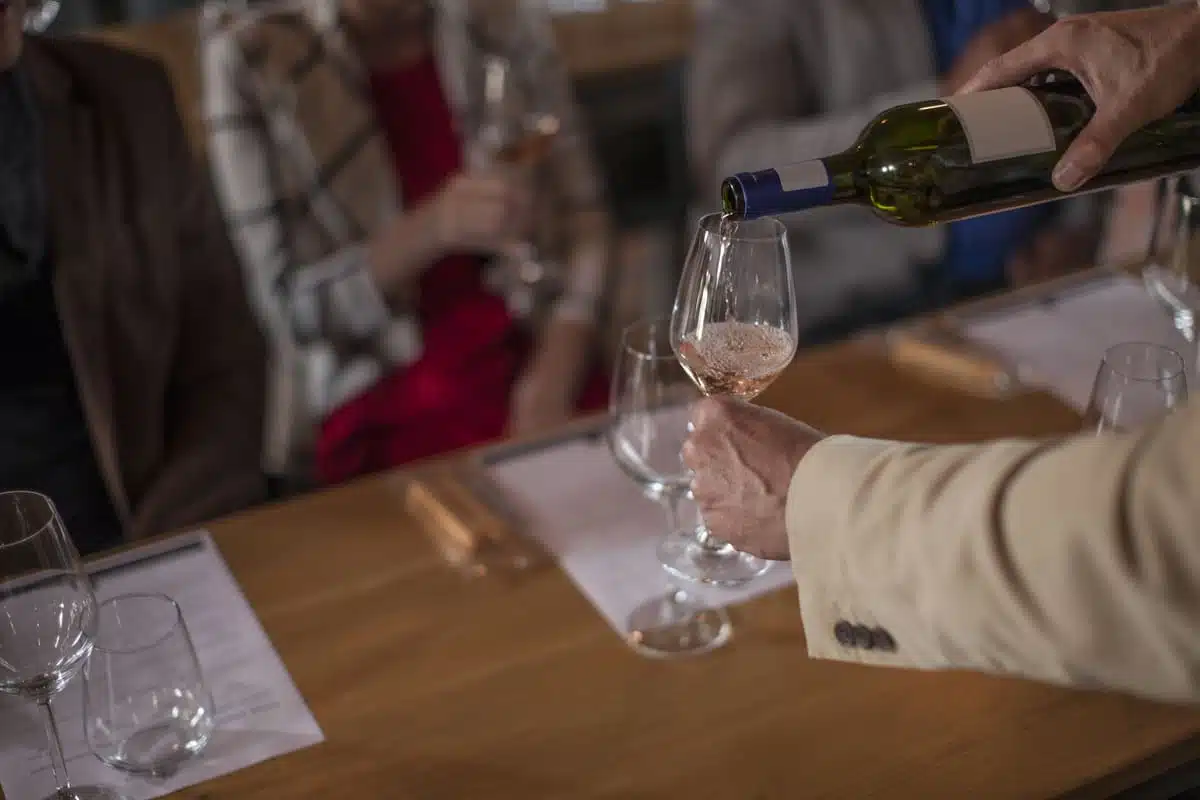wine being poured into glass in front of people sitting at table